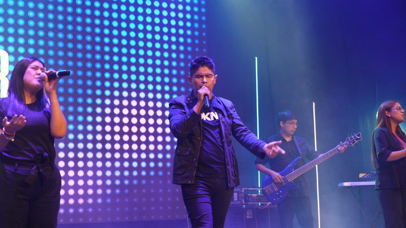 Dos vocalistas de Dfive cantando frente a una pantalla de luces