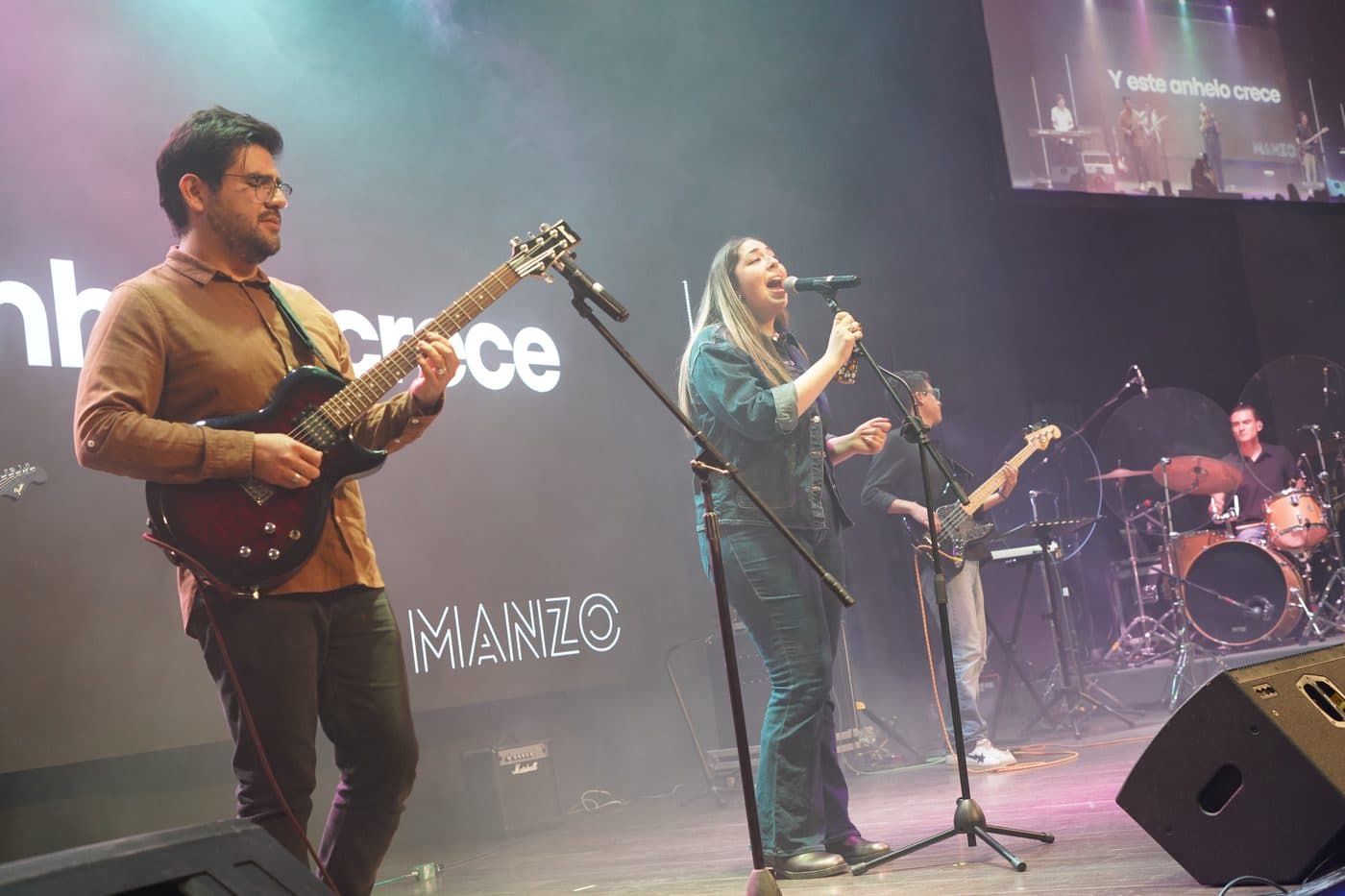 Manzo en el escenario: una vocalista y un guitarrista frente a la pantalla con el nombre de la banda