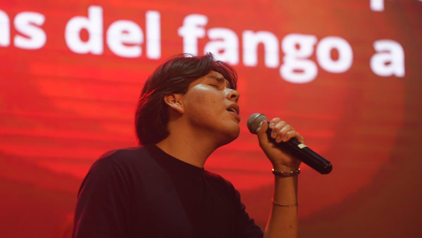 Un integrante de Shejiná cantando con los ojos cerrados bajo luces rojas
